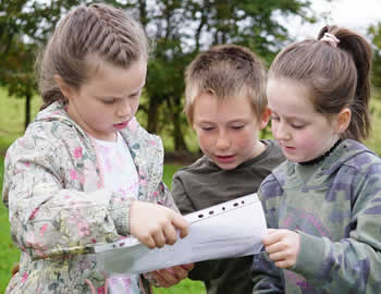 3 pupils looking at question on sheet of paper in grounds of St Aidans NS Ballintrillick
